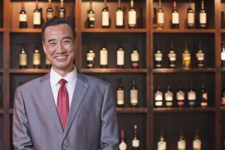 Smiling Businessman Standing by Wine Bottles, Portraitの写真素材