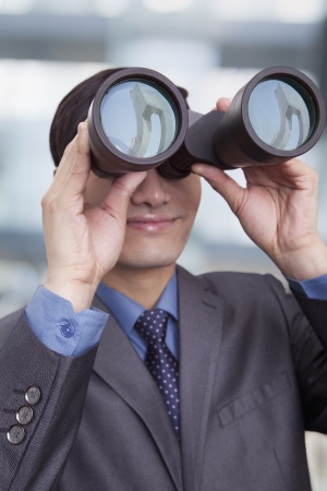 Young businessman looking through binoculars, Beijingの写真素材