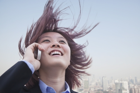 Young businesswoman smiling using her cell phone with hair blowingの写真素材