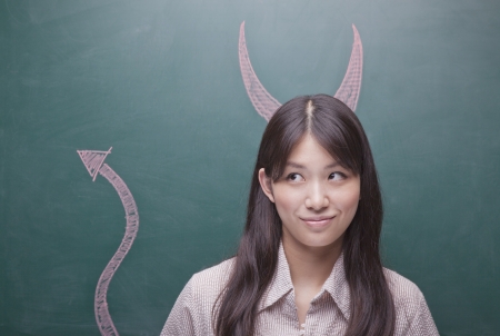 Young woman with devil horns and tail on blackboardの写真素材