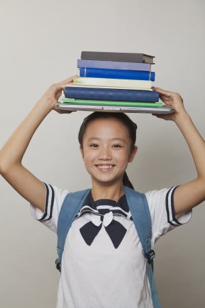 Girl smiling and holding bunch of notebooks and laptop on her head, Studioの写真素材
