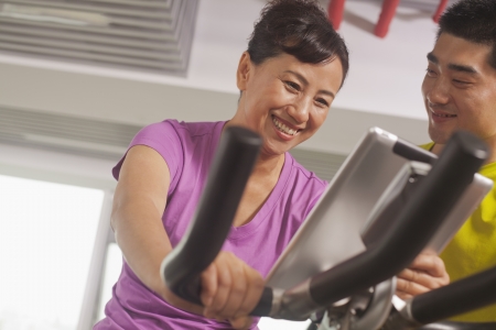 Woman smiling and exercising on the exercise bike with her trainerの写真素材