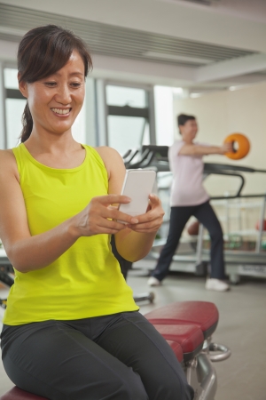 Mature woman using her cell phone in the gym の写真素材