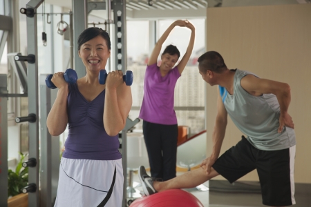 mature woman lifting weights in the foreground, people exercising in the backgroundの写真素材
