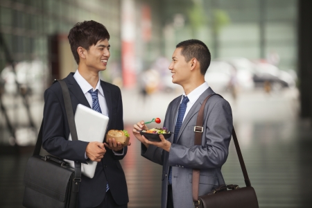Two young businessmen talking and having a lunch outdoorの写真素材