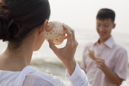 Young couple looking at seashells, holding shell to ear の写真素材