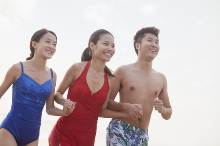 Three friends holding hands and smiling on the beachの写真素材
