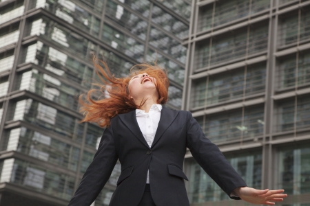Excited young businesswoman looking up with wind blowing in her hairの写真素材
