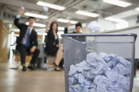 Three coworkers preparing to throw paper into waste basket の写真素材