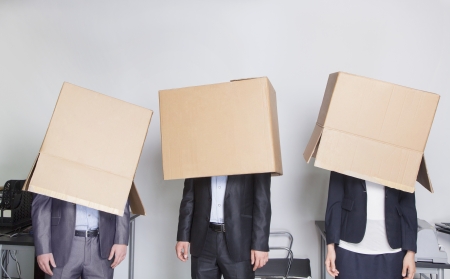 Three business people with boxes over their heads in an officeの写真素材