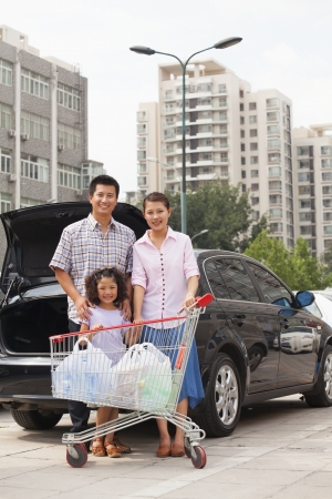 Family with shopping cart standing next to the carの写真素材