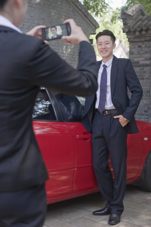 Businesswoman Taking Businessman's Picture Next to His Carの写真素材