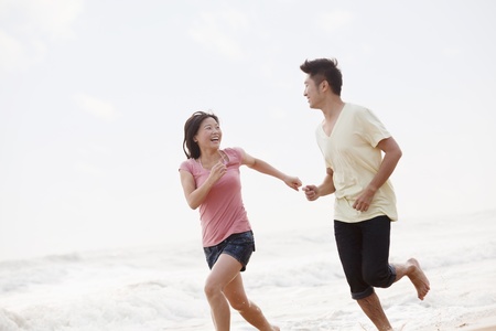 Couple running by the waters edge on the beach, Chinaの写真素材