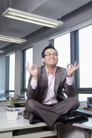 Businessman sitting on desk in the office meditating の写真素材