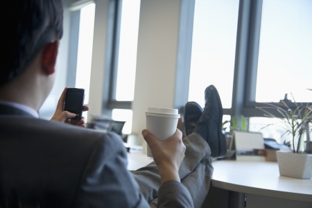 Businessman with feet up drinking coffee and text messagingの写真素材