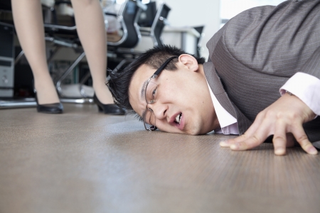 Businessman with face on the floor, coworker standing by himの写真素材