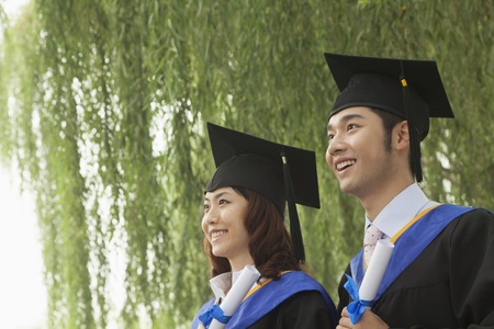 Two Young University Graduates Holding Diplomas And Looking Away の写真素材