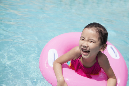 Portrait of a cute little girl swimming in the pool with a pink tube