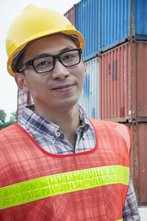 Portrait of smiling young engineer in protective workwear outdoors in a shipping yardの写真素材