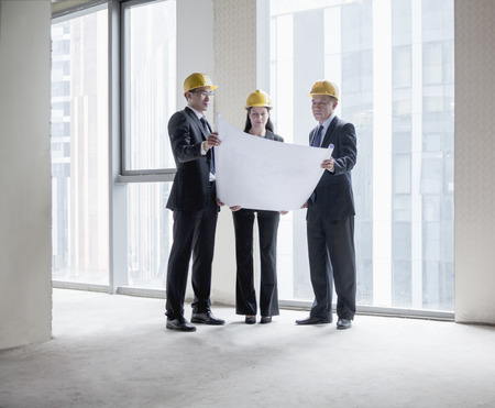 Three architects in hardhats examining a blueprint in an office buildingの写真素材