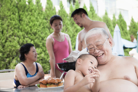 Smiling multi-generational family barbequing by the pool on vacationの写真素材