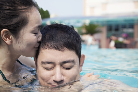 Woman with eyes closed kissing man on the cheek in the water in the poolの写真素材