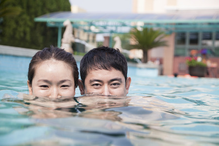 Happy couple with face half underwater in the pool looking at cameraの写真素材