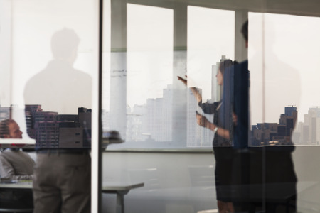 Four business people standing and looking at a white board on the other side of a glass wallの写真素材