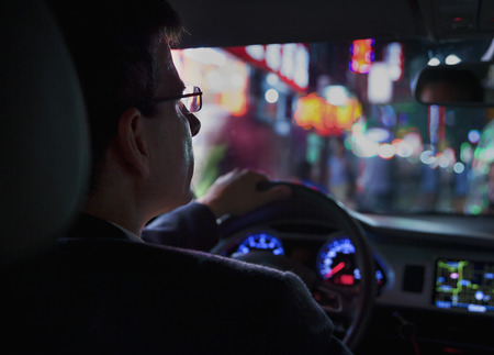 Over the shoulder view of businessman driving at night in the city, illuminated city lightsの写真素材