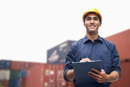 Smiling young engineer in protective work wear in a shipping yard examining cargoの写真素材