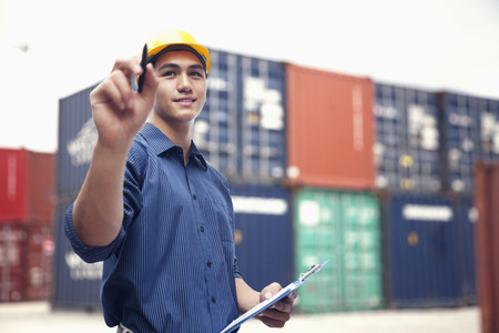 Smiling young engineer in protective work wear in a shipping yard examining cargoの写真素材