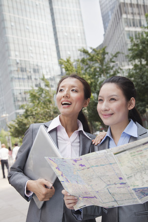 Two young businesswomen with the map looking for location の写真素材