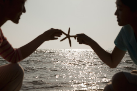 Silhouette of mother and daughter holding a starfish on the beachの写真素材