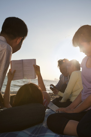 Multigenerational family relaxing and reading on the beachの写真素材