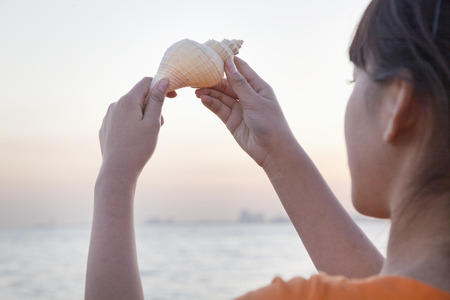 Teenage girl looking and holding up seashellの写真素材