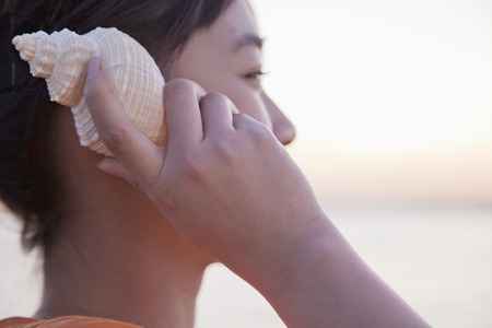 Teenage girl listening to seashell, close-upの写真素材