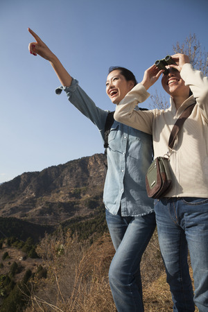 Women hiking, using binoculars, pointing at the mountain top の写真素材