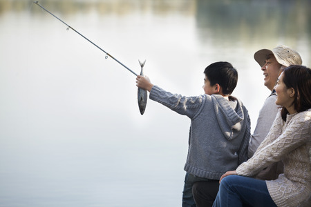 Boy admiring fishing catch with family at lakeの写真素材