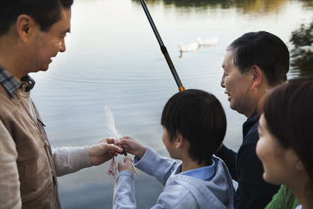 Family teaching a boy how to fish at a lakeの写真素材