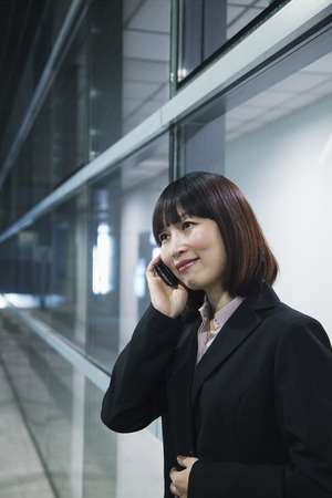 Businesswoman using the phone by a glass wall, Beijingの写真素材