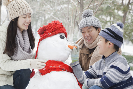 Family making snowman in a park in winterの写真素材
