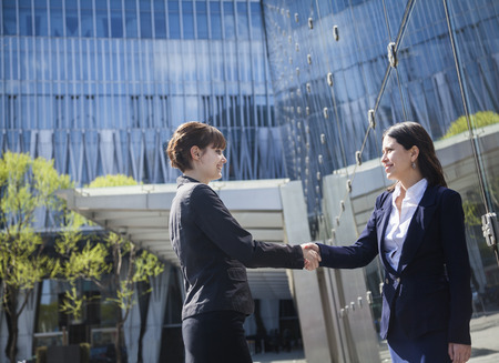 Two smiling young businesswomen shaking hands outdoors in Beijing, Chinaの写真素材