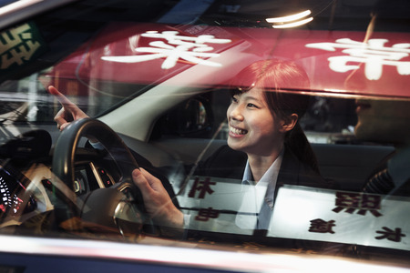 Smiling businesswoman pointing out of the car while driving through Beijing at nightの写真素材