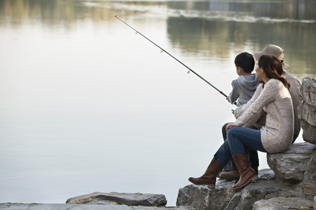 Family fishing off of rocks at lakeの写真素材