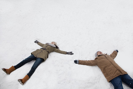 Young couple laying in snow making snow angelsの写真素材
