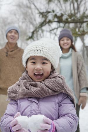 Young girl carrying snow balls in front of parents in park in winterの写真素材