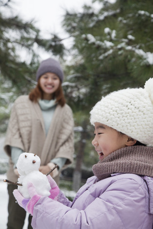 Girl Holding a snowman in a park with motherの写真素材