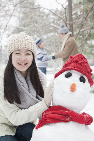 Mother making snowman in park in winterの写真素材