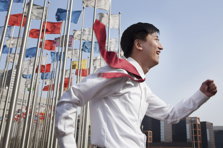 Businessmen running and smiling with flagpoles in background.の写真素材