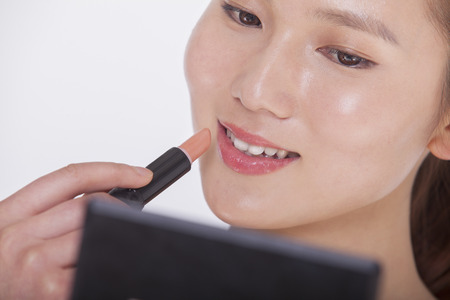 Close up of young woman applying lipstick in a mirror, studio shotの写真素材